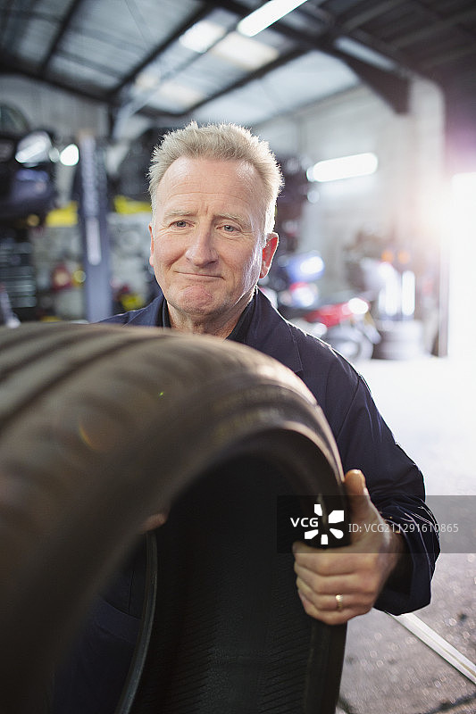 男性技工在汽车修理店持有轮胎图片素材