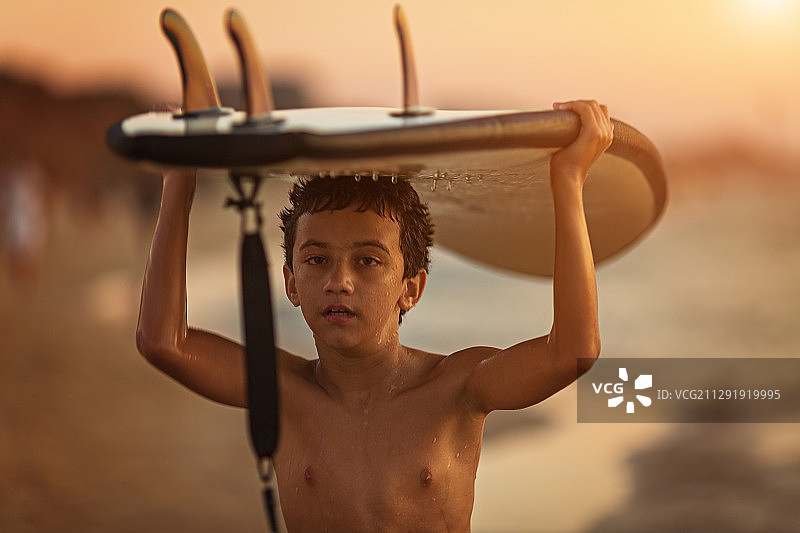 赤膊小男孩(10-11岁)在日落时举着冲浪板图片素材