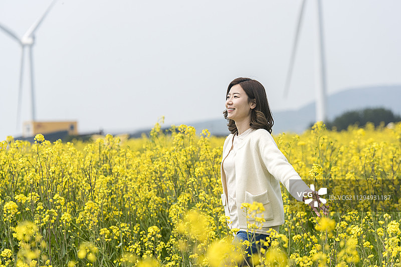 女人享受时间在油菜花田旁边的风力涡轮机图片素材