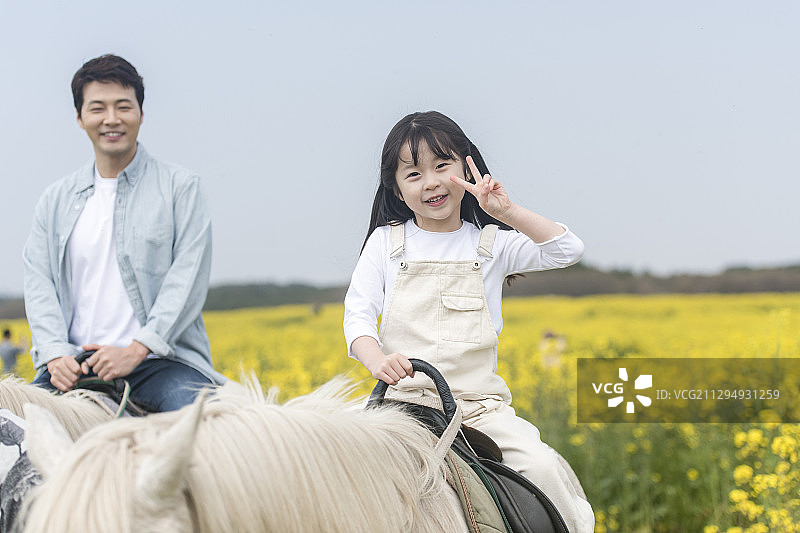 父亲和女儿做手势，骑在油菜花圃旁图片素材