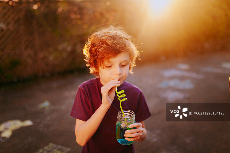 可爱的男孩站在路上用可重复使用的吸管喝水，维多利亚，加拿大图片素材
