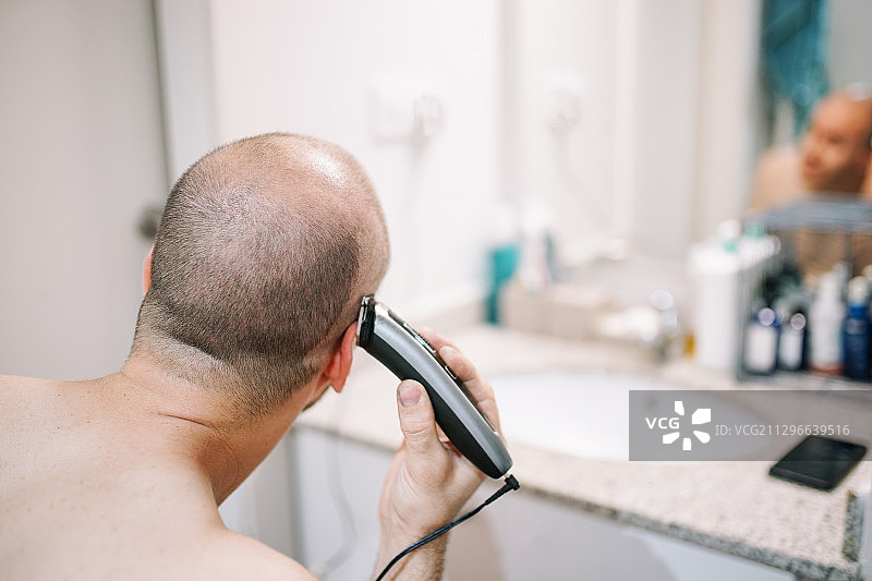 西班牙莱莱达，一名男子在浴室里用电动剃须刀剃头图片素材