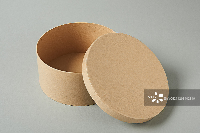 棕色的圆形硬纸盒，盖子打开，背景为灰色图片素材