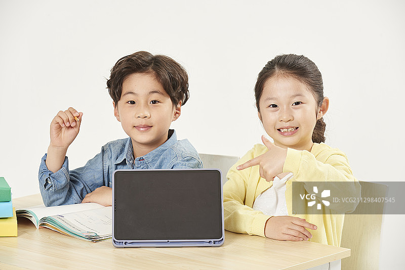 男孩和女孩坐在桌子旁，指着一个数字平板电脑图片素材