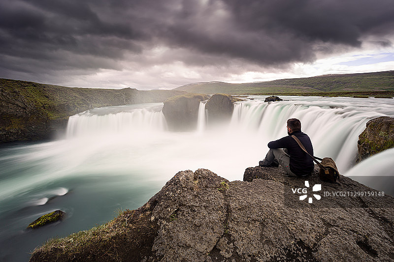 冰岛拉格尔，一名男子坐在瀑布前的岩石上图片素材