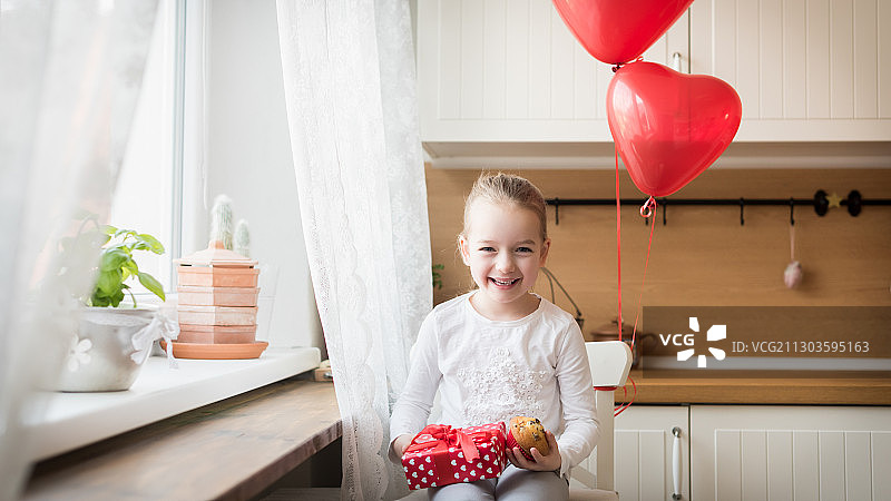 斯洛伐克，一个微笑的女孩拿着气球，靠墙站在家里图片素材