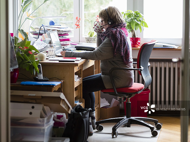 女人在拥挤的家庭办公室里用笔记本电脑工作图片素材