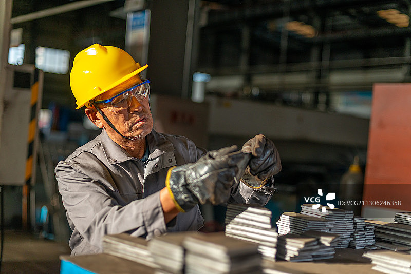 阳光下厂房里带安全帽检查零件的技术工人图片素材
