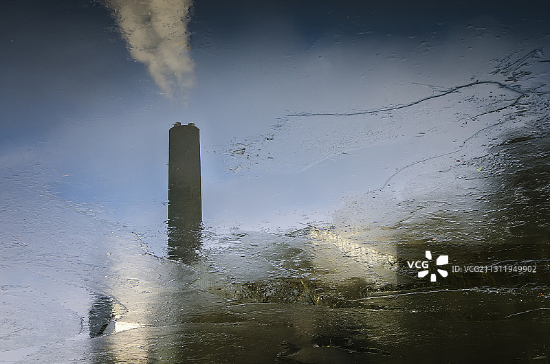 工厂的烟囱倒映在冰冷的运河水里。图片素材