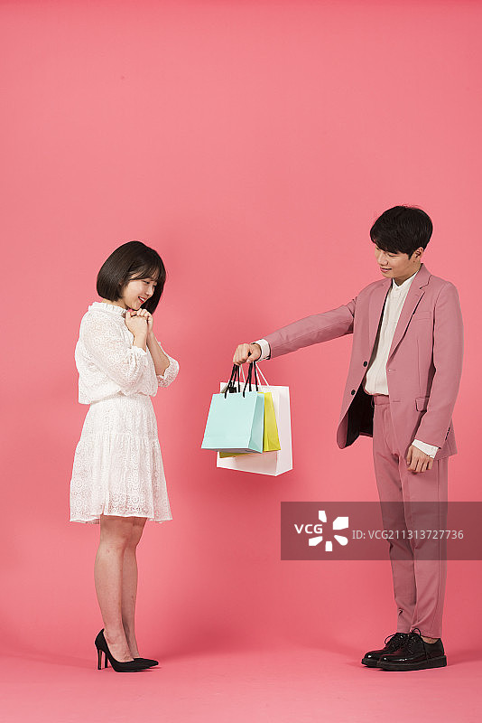 一名男子将购物袋送给粉色背景的女子图片素材