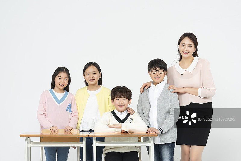 老师和四个孩子坐在和站在课桌旁微笑图片素材