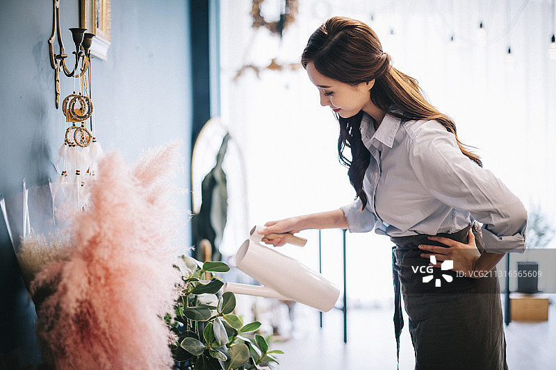 花店的花匠用喷壶在花店里把手放在地上浇花图片素材