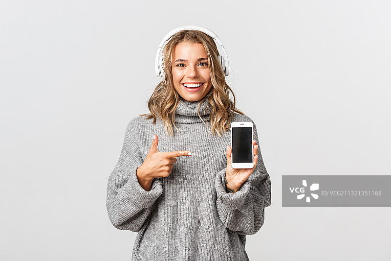 微笑的年轻女子的肖像听音乐，同时拿着手机对白色的背景图片素材