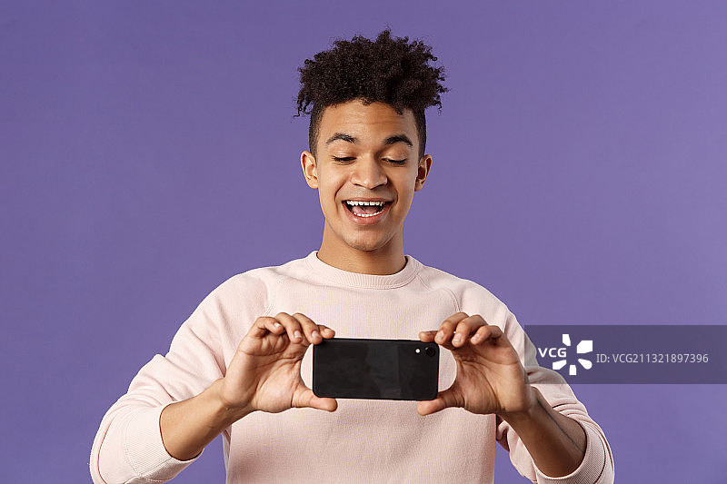 在紫色背景下用手机微笑的男人图片素材