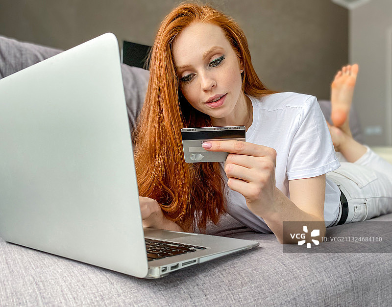 年轻的红发女人用笔记本电脑和信用卡在网上购物图片素材