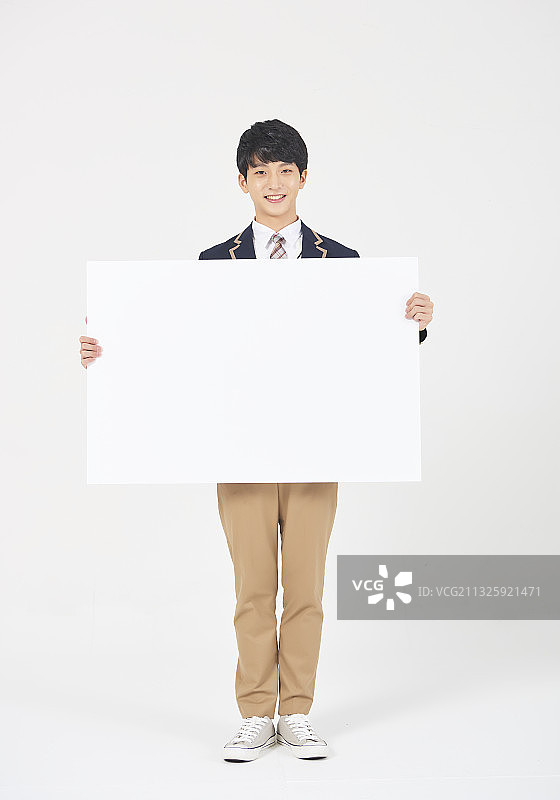 十几岁的男孩穿着制服，手持白色背景上的空白横幅图片素材