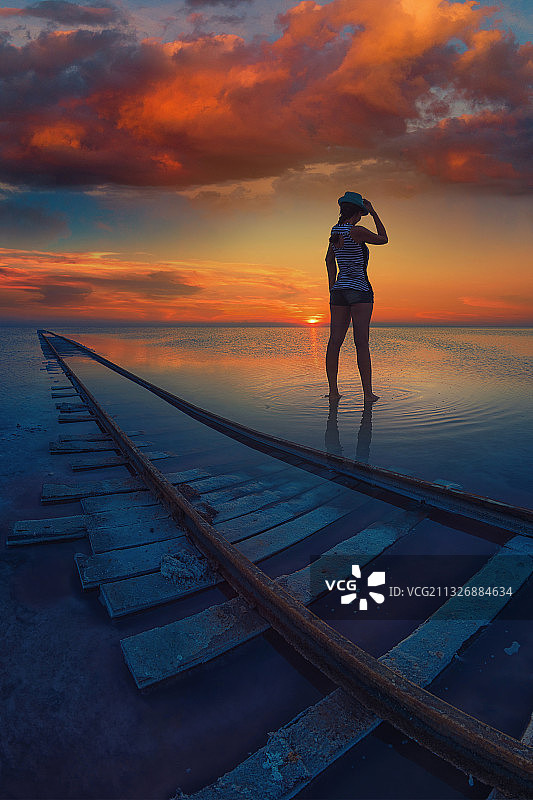 后视图的女人站在铁路在海滩上对天空日落图片素材