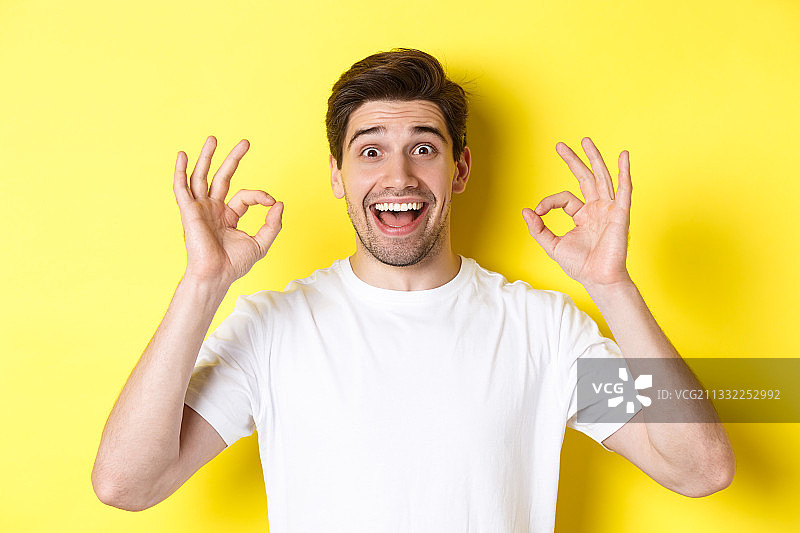 一个微笑的男人站在黄色背景下打手势的肖像图片素材