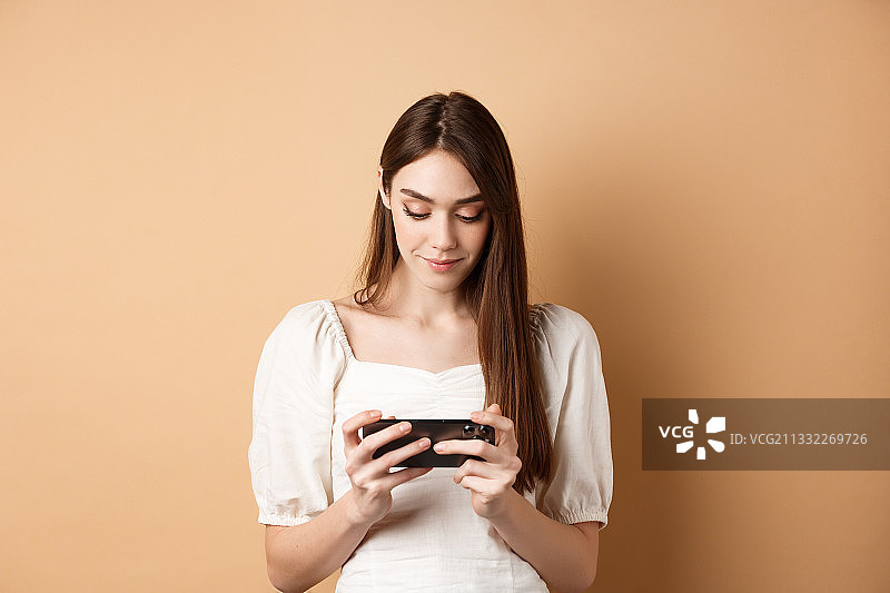 一名年轻女子站在棕色背景下使用手机图片素材