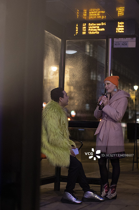 时髦的年轻夫妇晚上在城市公交车站聊天图片素材