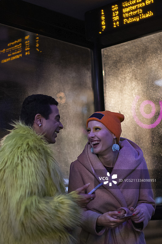 幸福时尚的情侣晚上在城市公交车站用智能手机图片素材