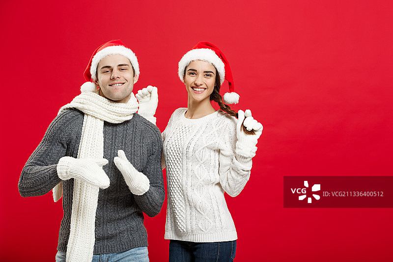 微笑的朋友戴着圣诞老人的帽子，站在红色的背景图片素材