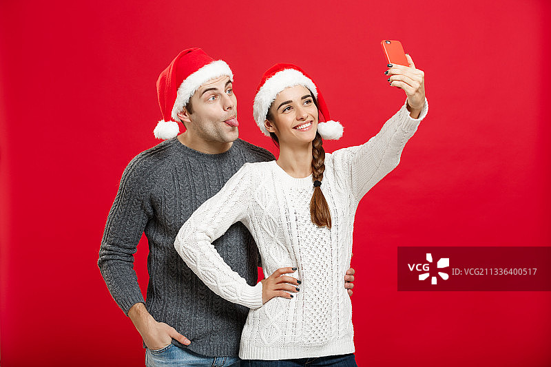 年轻夫妇戴着圣诞老人帽，站在红色背景下图片素材