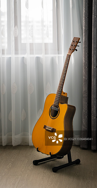 窗户前静静的吉他。白色的窗帘，竖在地上架子上的桔色的吉他。图片素材