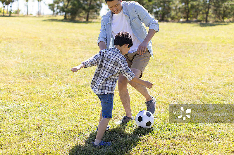 快乐的父子俩在草地上踢足球图片素材