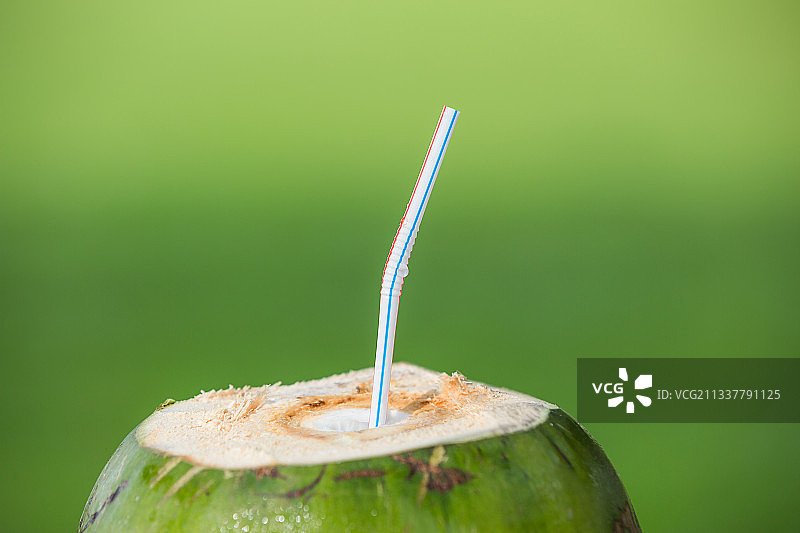 户外绿色背景前插着吸管的椰子。图片素材