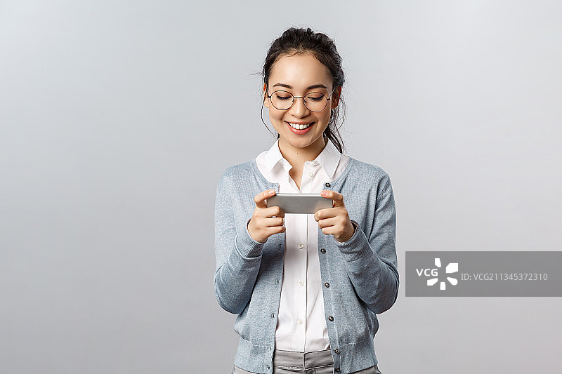 微笑的年轻女子在灰色背景下使用手机图片素材