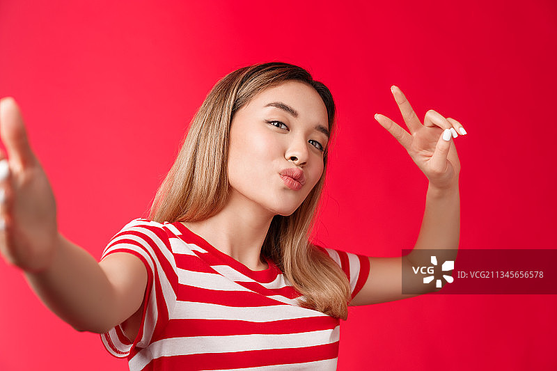 年轻女子的肖像在红色背景下做和平手势图片素材