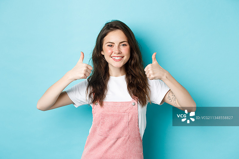 微笑的年轻女人的肖像手势向上在蓝色背景图片素材