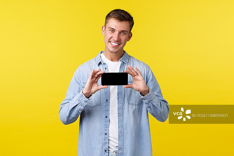 一名微笑的男子手持智能手机，站在黄色背景下图片素材