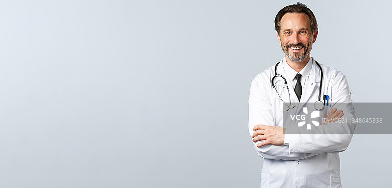 微笑的医生肖像，双臂交叉站在灰色的背景图片素材