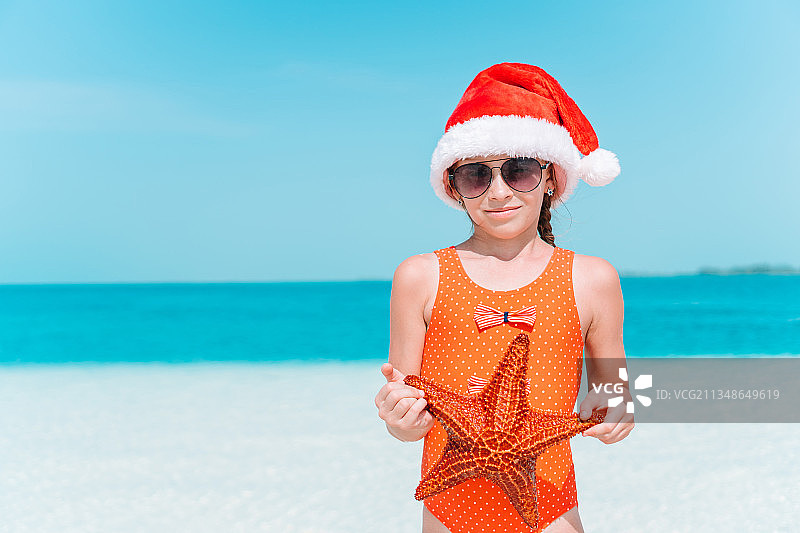 可爱的女孩戴着圣诞老人的帽子，站在天空的海滩上图片素材