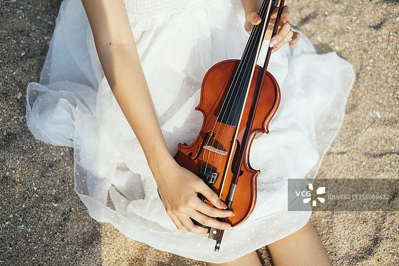 剪短的小提琴图像在沙滩上白色连衣裙女人的腿上。图片素材
