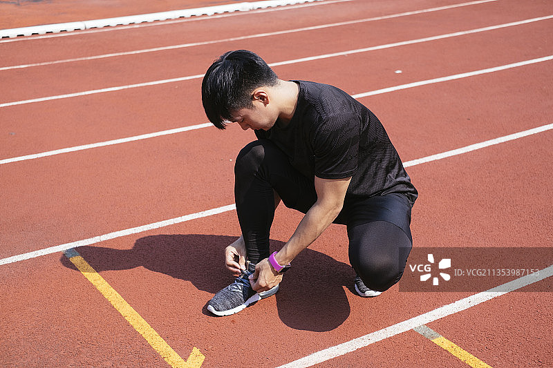 运动亚洲泰国男子在跑步后在跑道上穿黑色运动服系鞋带。图片素材