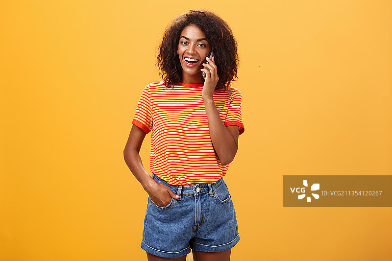 在橙色背景下，微笑的年轻女子的肖像在讲电话图片素材