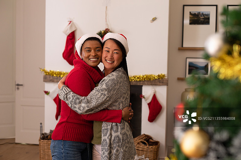 两个快乐的不同的女性朋友戴着圣诞帽在圣诞节拍照图片素材
