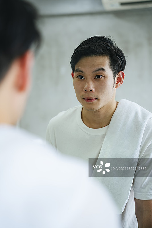 一个亚洲年轻人在浴室镜子里看着自己。图片素材