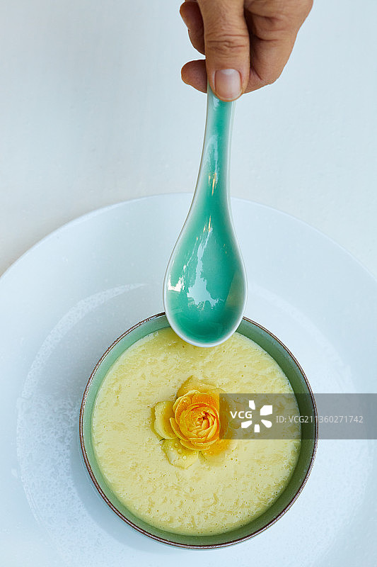 花园里白色餐桌上的一碗有黄色花朵的有机素食玉米羹图片素材