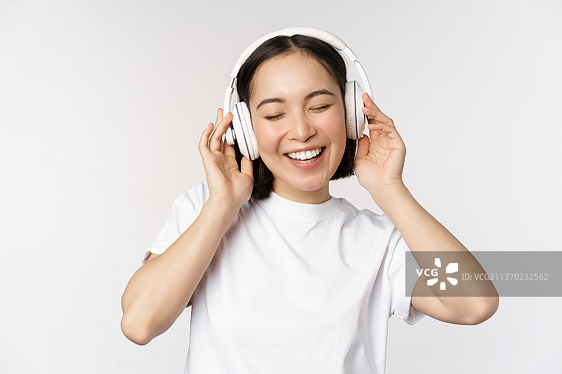 现代亚洲女孩跳舞，带着耳机听音乐，微笑图片素材