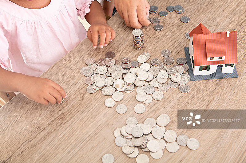 俯视桌子上一堆美元硬币和小房子模型及正在玩耍的小女孩图片素材