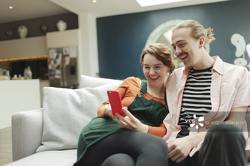 幸福的年轻夫妇在客厅沙发上玩智能手机图片素材
