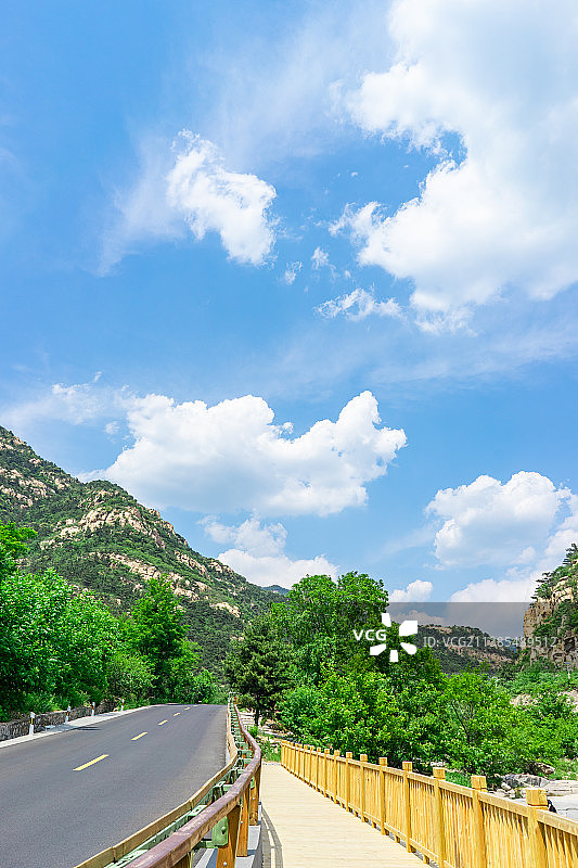 中国非都市风光拍摄主题，山东省泰安市岱岳区彩石溪风景区，绿色的山脉，蜿蜒的环山路，蓝天白云，步行道路图片素材