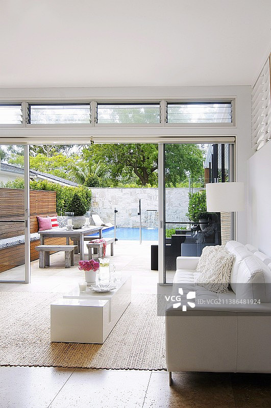 设计师客厅的角落，白色皮沙发和极简风格的低矮茶几，在开放式的露台门前，可以看到游泳池图片素材