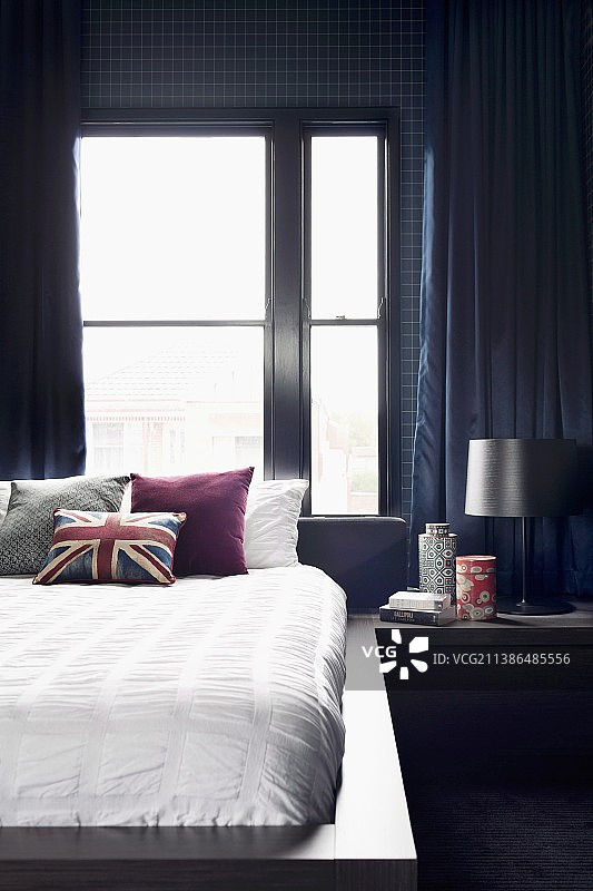 男性风格的卧室，深蓝色的壁纸和窗帘，白色的床上用品和英国国旗靠垫图片素材