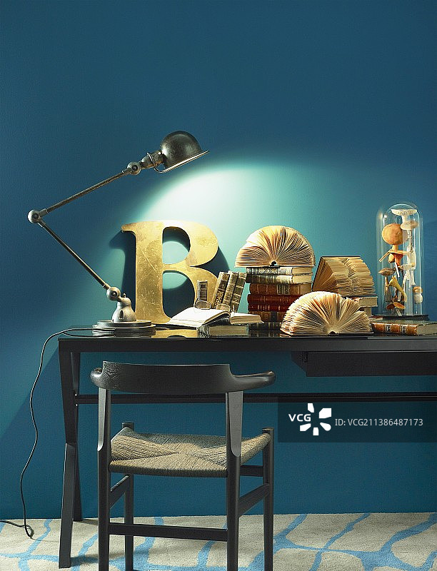 拼接的台灯，装饰性的字母和古籍书籍在书桌上对着蓝色的墙图片素材