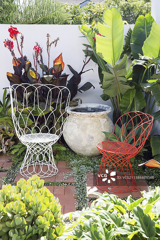 白色和红色的铁丝扶手椅坐在绿色的花园角落里图片素材